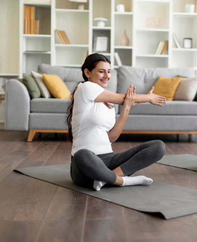 Femme adulte assis en tailleurs sur un tapis entrain de faire d'étirer ses bras