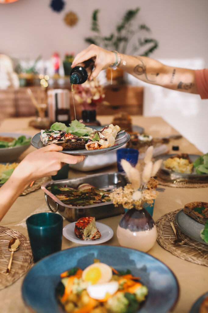 Table avec multiples plats et quelqu'un entrain de verser de l'huile sur une assiette