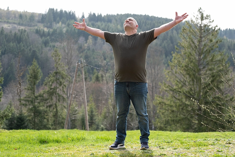 Homme levant le bras au ciel, heureux de participer à un séjour adapté